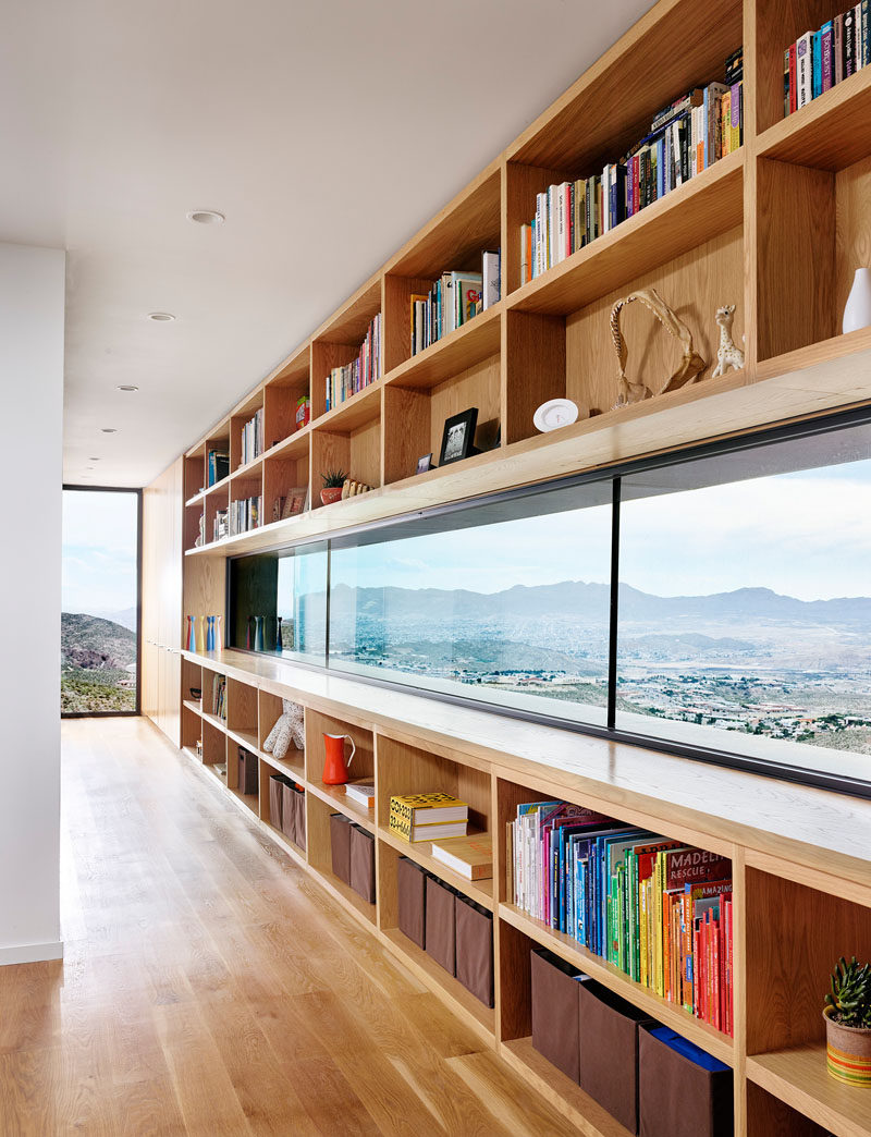 In this modern house, white oak open shelving surrounds a horizontal letterbox window, while the floor-to-ceiling window looks out on the landscape and city below