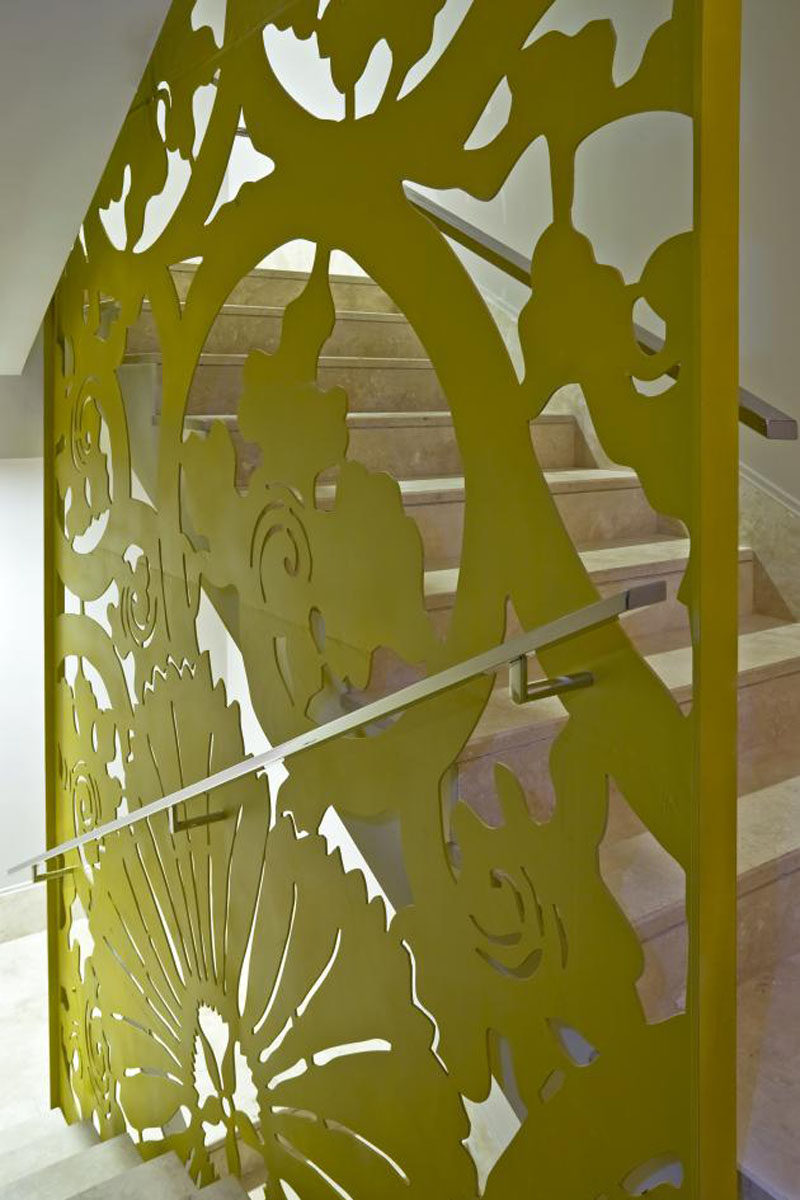 A sheet of metal has been laser cut and painted green to create an artistic floral print that doubles as both a safety railing for the stairs and an artistic installation to look at while you go up and down the stairs.