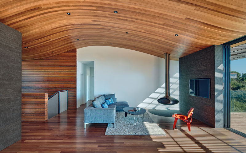 The wood ceiling in this modern living room with a hanging fireplace, mimics the shape of the hill the home sits on. 