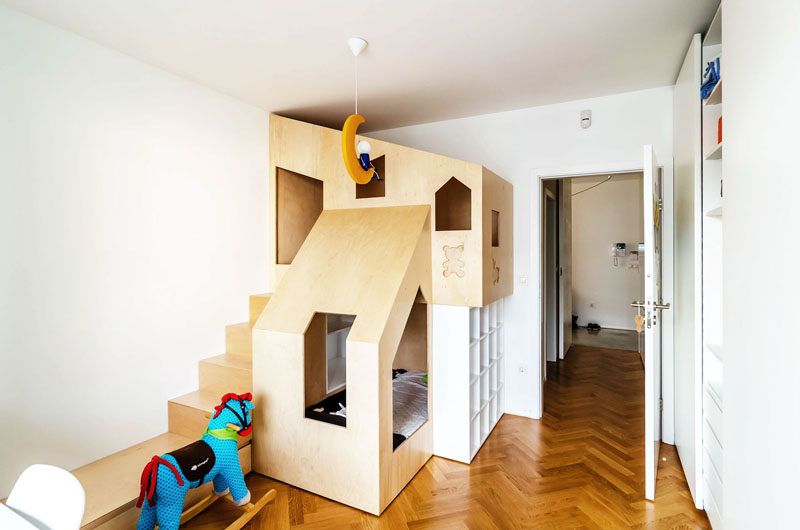 This custom modern plywood bunk bed design in a small kids bedroom houses two beds, a small bookshelf and features multiple wooden cutouts to create windows that allow light into the sleeping space and allows the little kids to look out from the comfort of their beds.