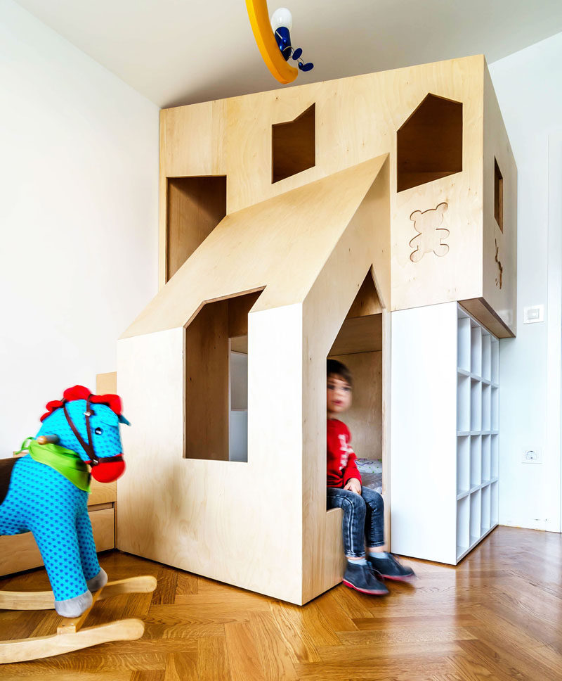 This custom modern plywood bunk bed design in a small kids bedroom houses two beds, a small bookshelf and features multiple wooden cutouts to create windows that allow light into the sleeping space and allows the little kids to look out from the comfort of their beds.