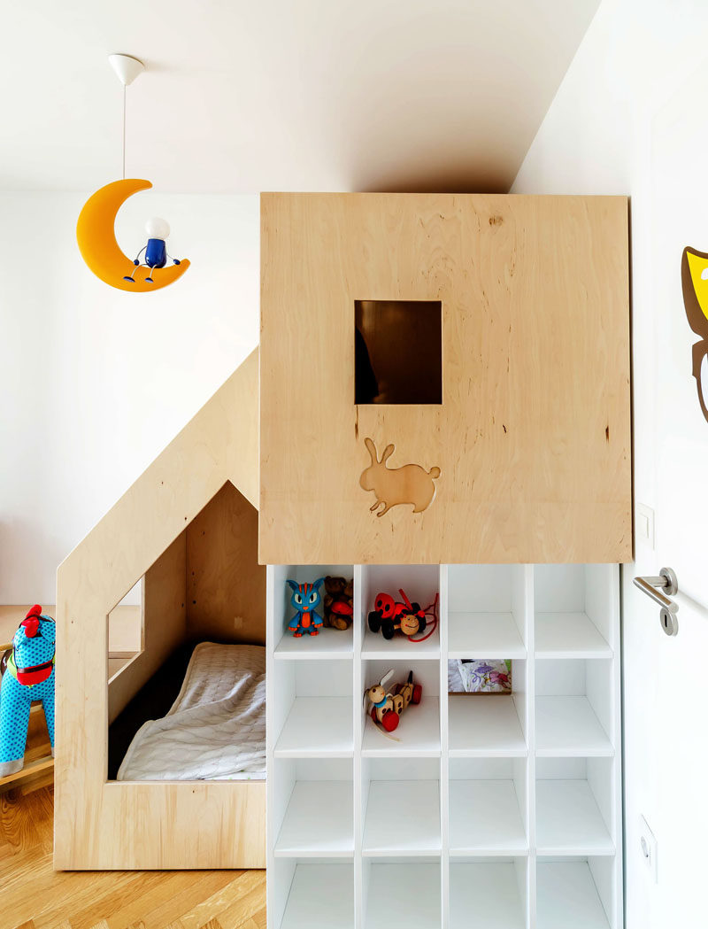 This custom modern plywood bunk bed design in a small kids bedroom houses two beds, a small bookshelf and features multiple wooden cutouts to create windows that allow light into the sleeping space and allows the little kids to look out from the comfort of their beds.