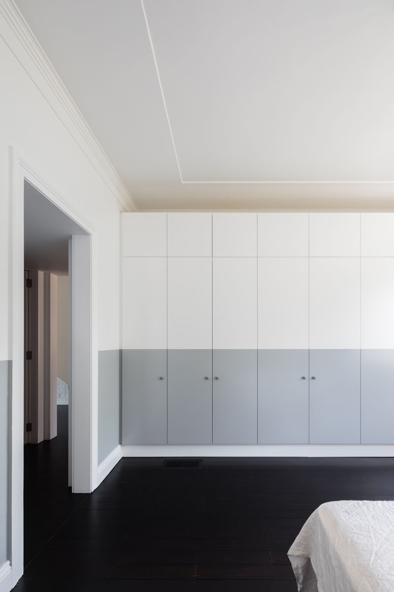 A wall of grey and white cabinets in this modern bedroom, provides plenty of storage space and keeps the room clutter free.