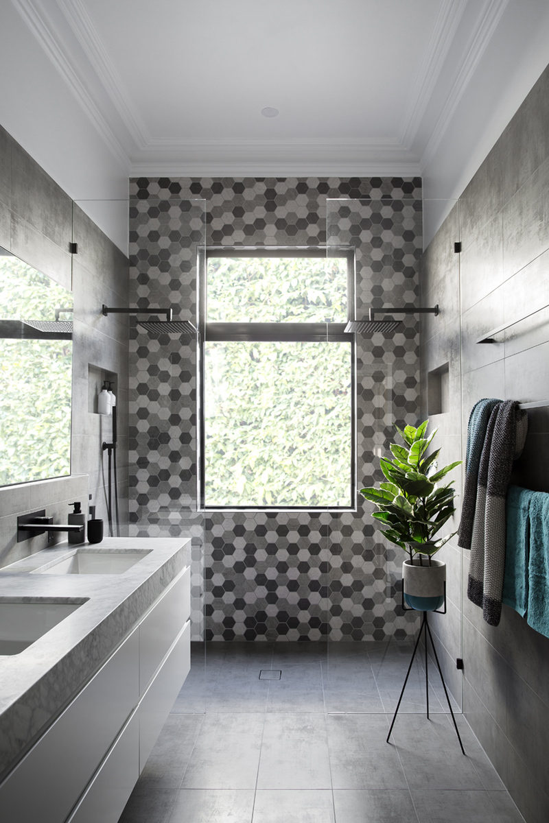 In this modern bathroom, the grey and white double vanity provides ample space for two people to get ready in the mornings, and the grey wall tiles match those on the floor and compliment the hexagon tiles on the wall in the two-person shower.