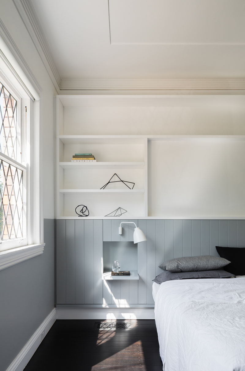 In this modern bedroom, a grey strip wraps around room and turns into the headboard behind the bed. A white shelving system above the bed provides extra storage and display room for decorative items and family photos. A small built-in shelf becomes a bedside table.