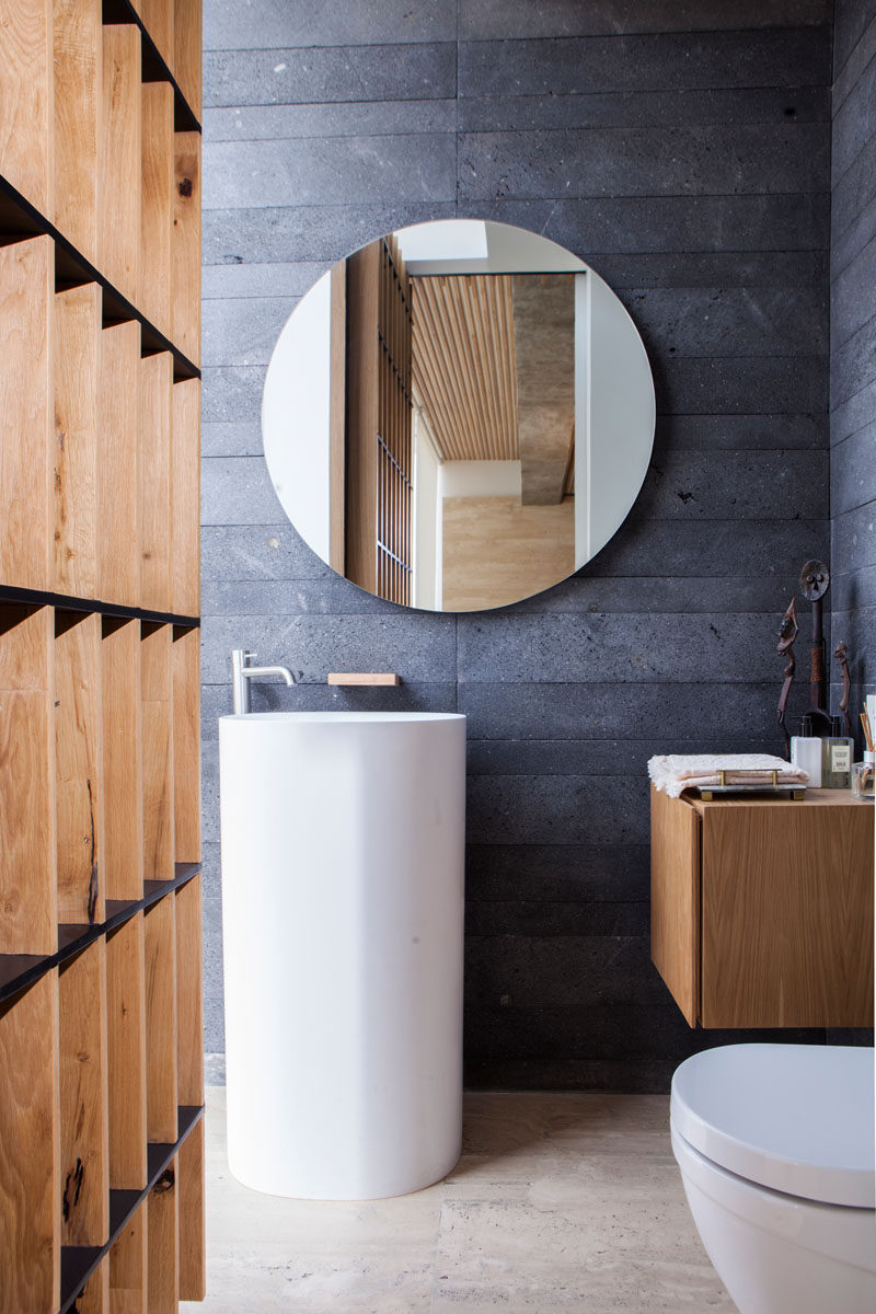 This modern bathroom features dark grey tiles and wood that have been paired with a simple standalone white basin and toilet.