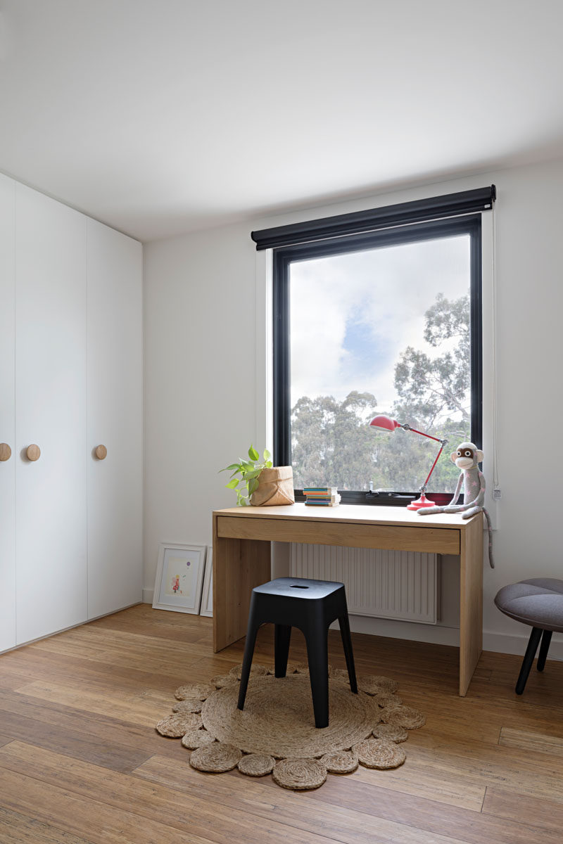 This kids bedroom has a small wood desk positioned in front of the window, perfect for daydreaming and floor-to-ceiling white cabinets have round wood door handles to match the wooden floor and desk.