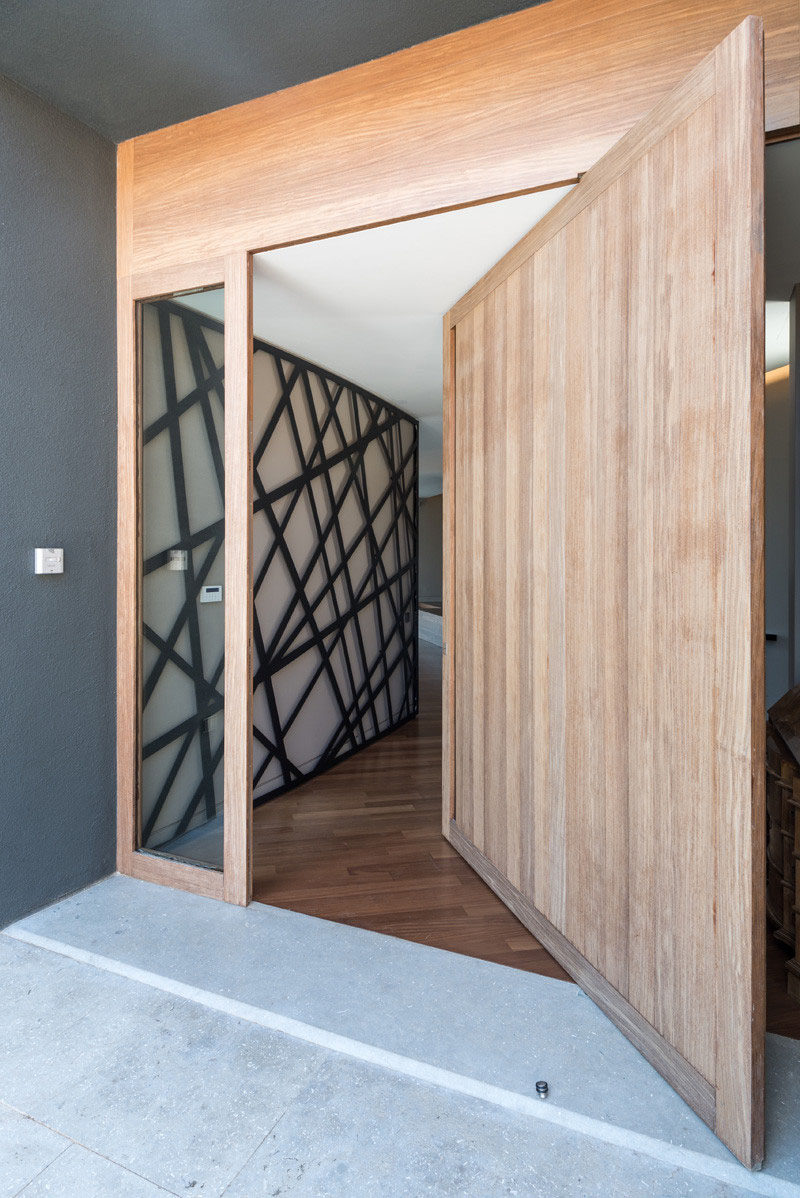 A large light wood pivoting door greets people at the front of this modern Greek home.