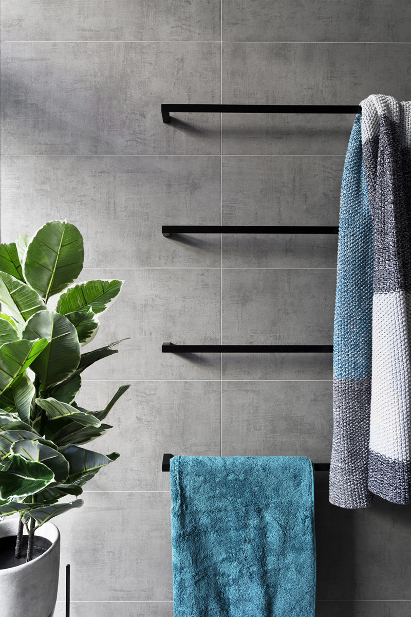 In this modern grey and white bathroom, matte black accents like towel bars add a sophistication to the bathroom, while the touches of blue in the towels and green in the plant add a pop of color to the otherwise neutral space.