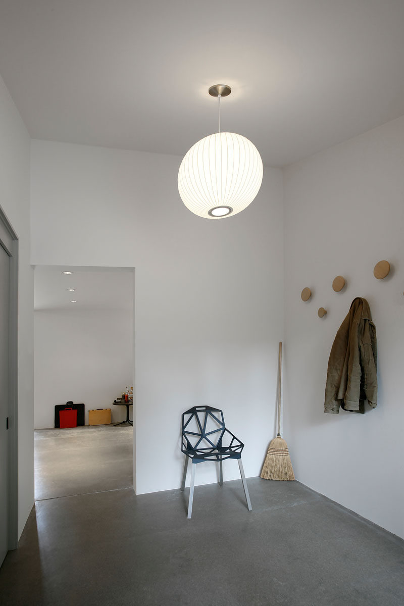 This minimalist white mud room in a renovated stable has just the essentials - a few wall hooks, a chair to make it easier to put on your shoes, and a broom for wiping up messes tracked in from outside. There's also a closet for storing coats, and a single pendant light and provides enough lighting in the room to keep it bright.