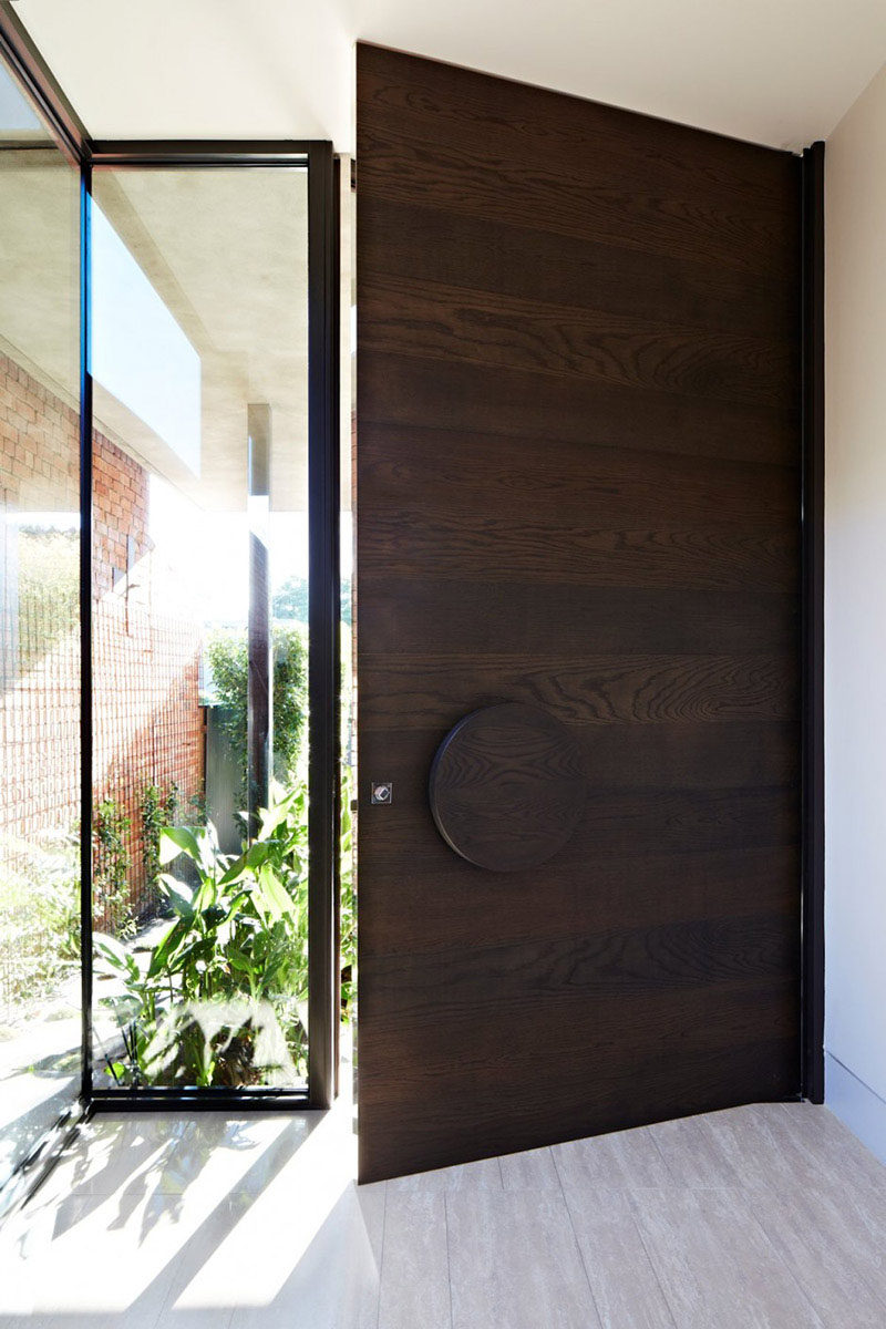 This large dark wood door with the wood grain running horizontally features an oversized circular handle that gives the entry way a modern feel.