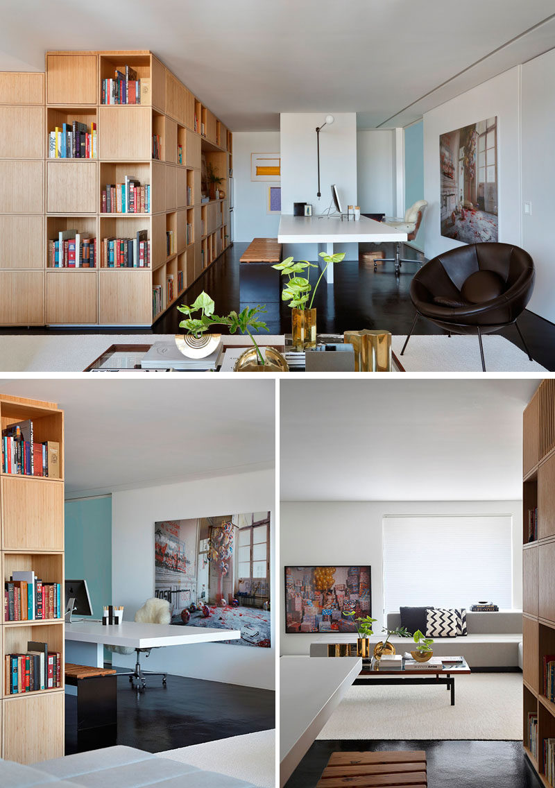 This modern apartment has a home office with a central work table and a bench for seating. A wall of light wood cabinets and open shelving provides plenty of storage.