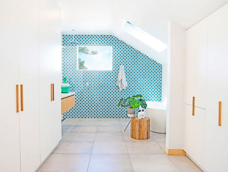 The most attention grabbing aspect of this mostly-white modern bathroom is the bright blue and white patterned tile accent wall that works well with the large grey porcelain floor and the floating wood vanity and built-in closet.