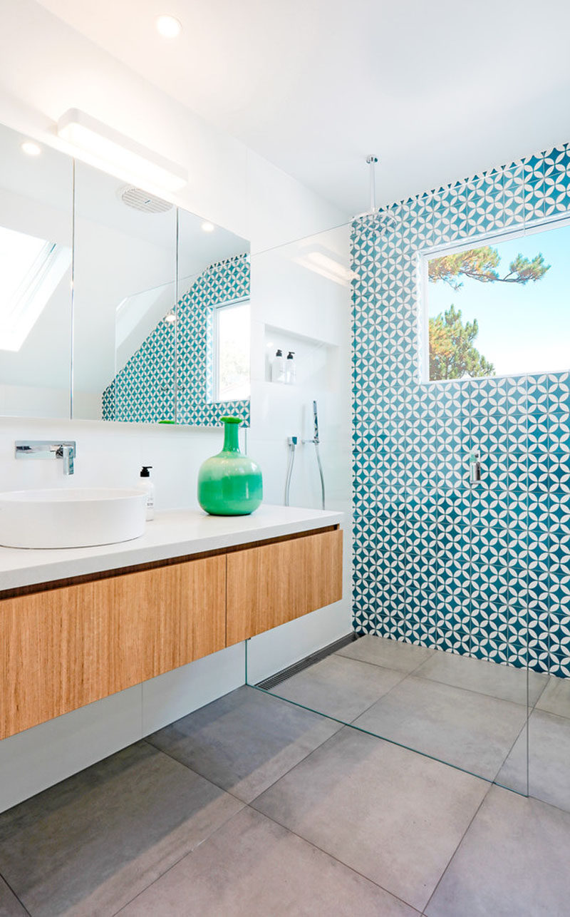 The most attention grabbing aspect of this mostly-white modern bathroom is the bright blue and white patterned tile accent wall that works well with the large grey porcelain floor and the floating wood vanity and built-in closet.