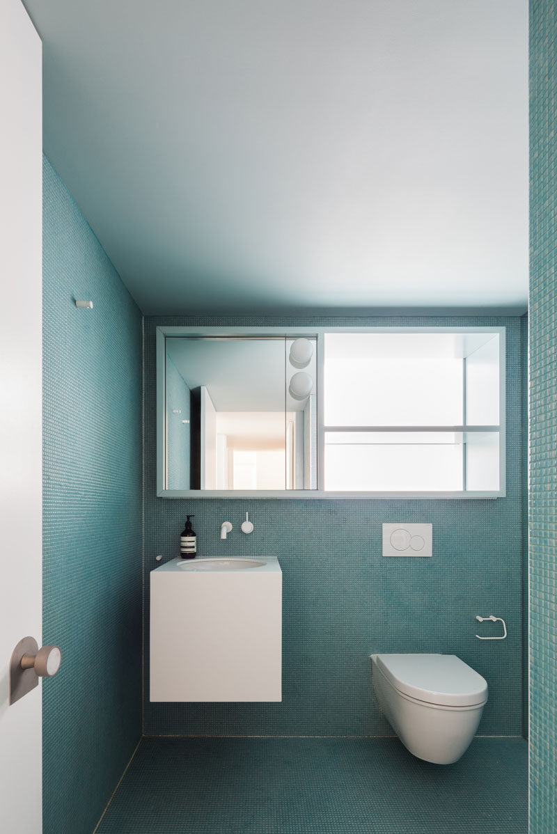 In this modern master bathroom, the tiny square turquoise tiles on both the walls and the floor create a monochrome look that's interrupted by the floating white vanity, the toilet and the large mirror that doubles as a storage cabinet.