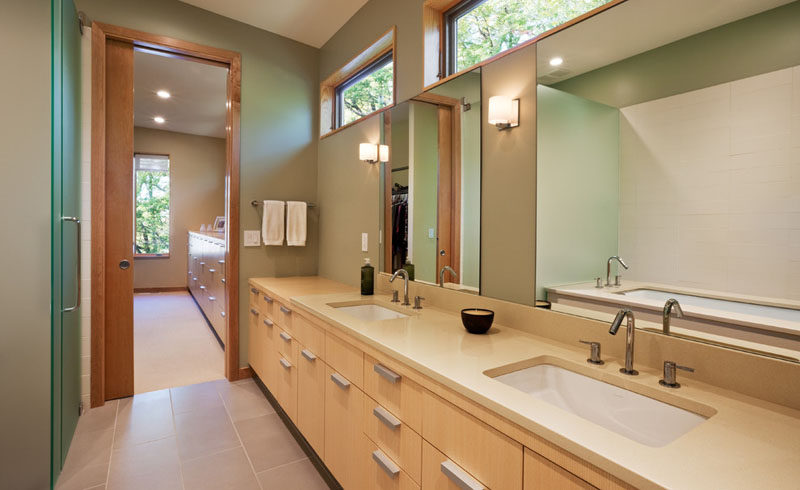 In this modern bathroom, windows along the top of the wall keep the space naturally bright, and a double vanity sink with lots of built in storage lets two people comfortably get ready at the same time.