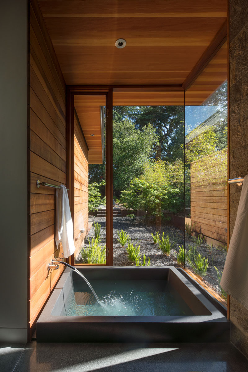 In the ensuite bathroom off the master bedroom in this modern house, is a private spa that's sunken down into the floor and looks out to the garden through the floor-to-ceiling windows.
