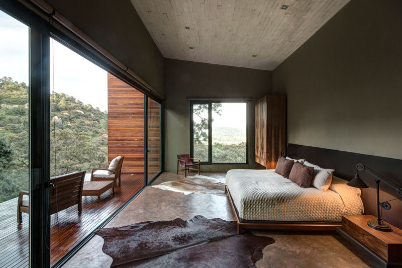 This master bedroom with a concrete ceiling, features a large sliding glass door that opens to provide access a private wood balcony.