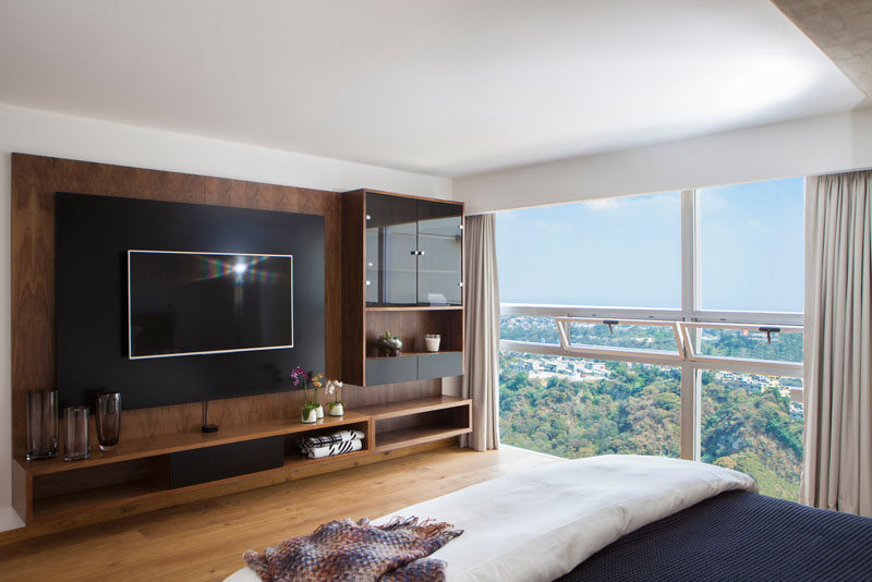 In this master bedroom, a custom wood entertainment unit with glass-enclosed shelves is the perfect place for displaying decorative items, while the large floor-to-ceiling windows are broken up by smaller windows that can be opened.