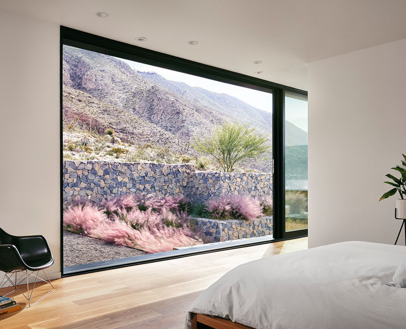 A large black framed sliding glass door opens up this master bedroom to the landscaped garden outside.