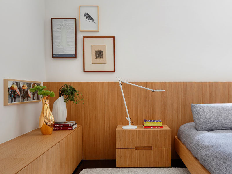 In this modern master bedroom, bamboo wood accents in the form of a sideboard, headboard, bed frame, and side table add a warmth to the space while art, plants, and books personalize it and give the room a cozy, welcoming feel.