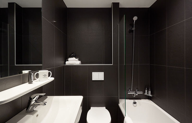 This modern black and white bathroom feature large black tiles and a white bath, vanity, toilet and shelf.