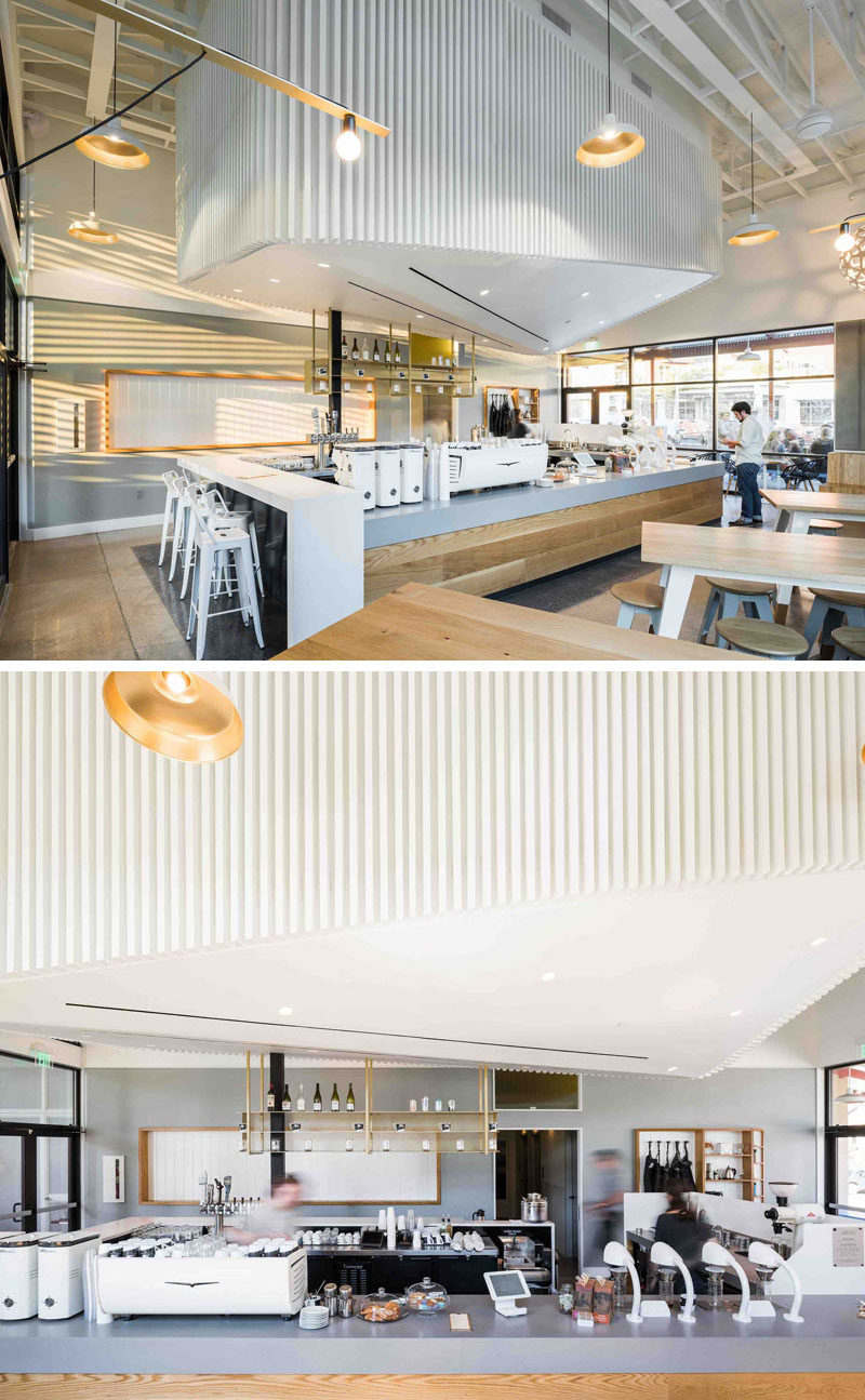 In this modern coffee shop, the service bar (or coffee bar) is central to the space, and the light grey countertop acts as a separation from the wood on the lower part of the bar and the white 'cloud' above.