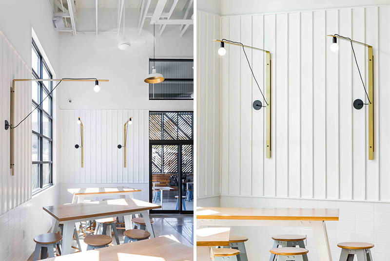 In this modern coffee shop, bar height tables and stools are positioned by the window, with simple metallic gold light fixtures adorning the walls.