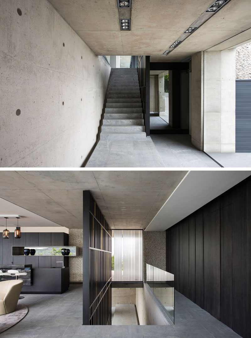 The entrance lobby of this modern house is surrounded by concrete walls and a matte black steel and bronze screen runs alongside the staircase leading to the main living level.