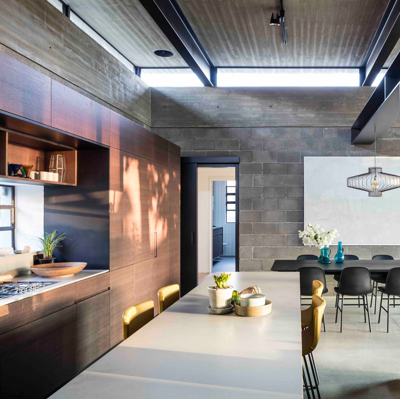 Behind the dining area and the living area in this modern house, is the kitchen. Wood cabinets without hardware keep the kitchen modern and streamlined, while the kitchen island with seating provides a more casual place to dine or help with meal prep.