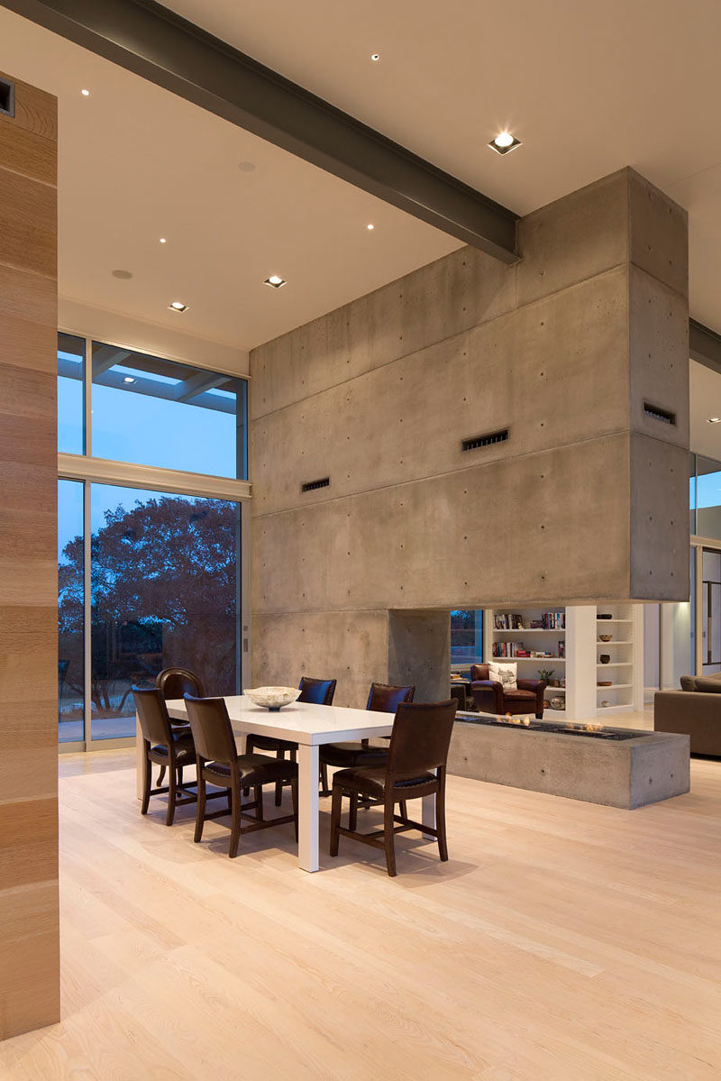 The dining room in this modern house features a tall ceiling and huge windows that work together to create an airy feel in the space while the concrete fireplace prevents the openness from feeling empty. Large steel I-beams that run through the house as well as the concrete add an industrial touch to the interior.