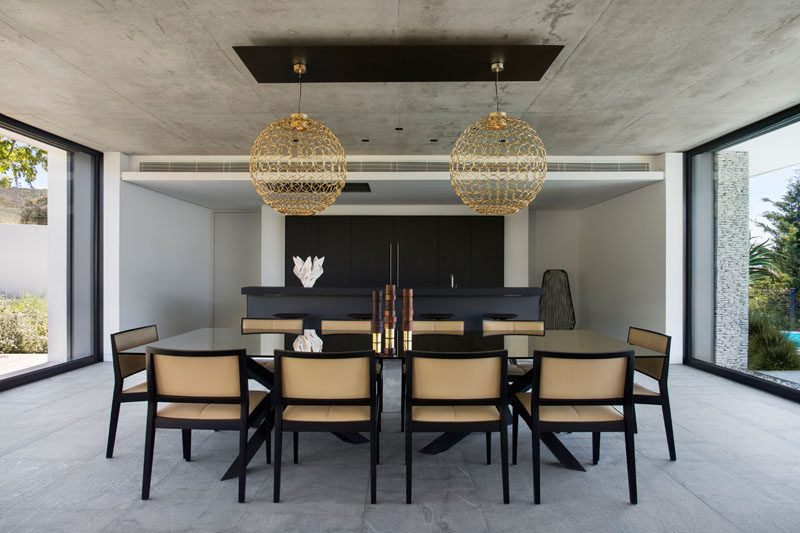 In this modern house, the matte black Bulthaup kitchen has been paired with a dark countertop, and shares the space with the dining room. Artistic gold pendant lights anchor the large dining table and chairs in the room.