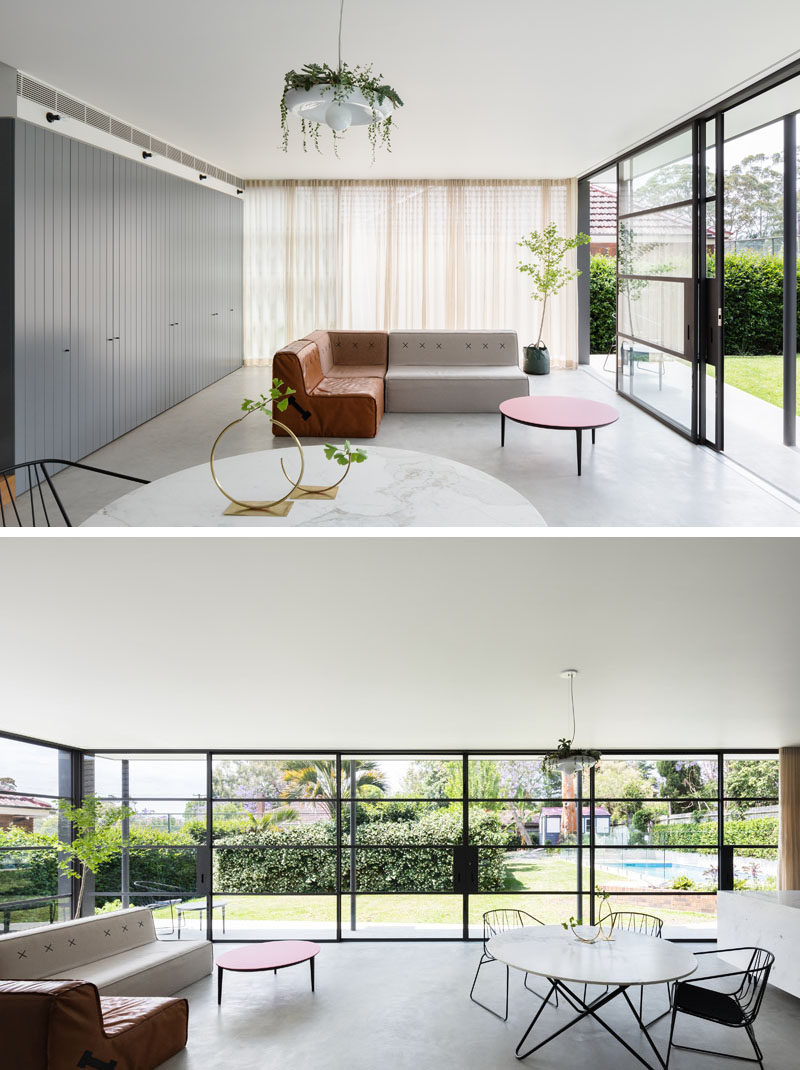 Inside the extension of this renovated house, wrap around black-framed windows make the combined living, dining, and kitchen area extra bright and connect the indoor and outdoor spaces. The grey concrete floor keeps the palette neutral and compliments the darker grey cabinets along the back wall.