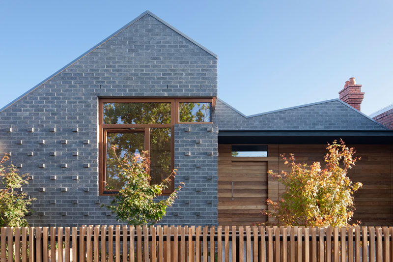 At the front of this modern house, a combination of grey brick and wood paneling covers the front exterior. Protruding bricks at the front add texture and depth, while the wood paneling that matches the trims of the windows and the fence adds warmth and a natural look to the home.
