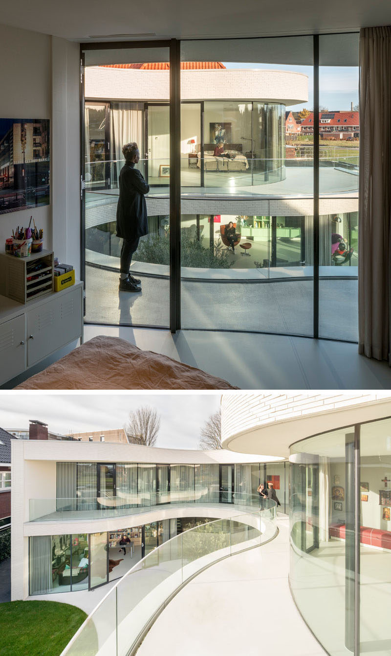 The floor-to-ceiling curved glass windows and doors on the upper floor of this modern house open up to the wraparound balcony.