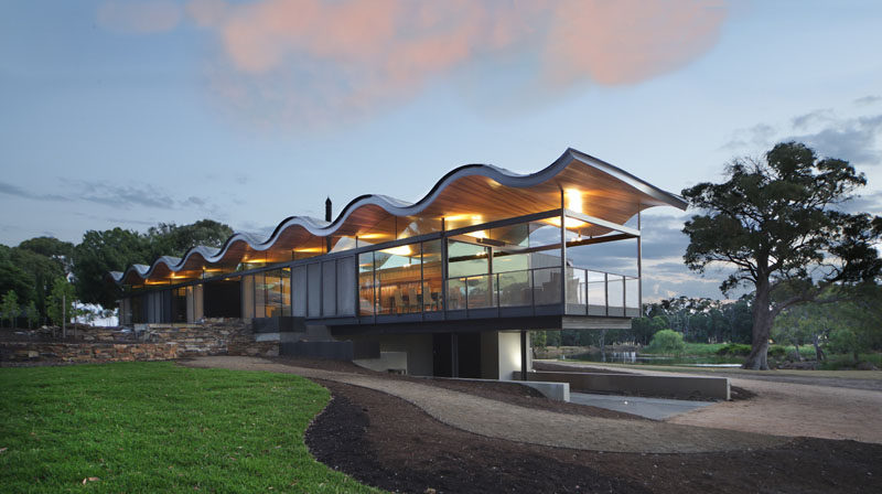 This modern house in Australia features a sculptural and wavy roof made from metal and wood, that's been designed to mimic the rolling hills surrounding the home.