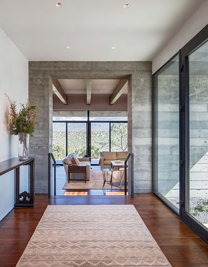 Stepping inside this modern house, there's a foyer with large windows that leads to the living room. From this angle, you can see part of a board-formed concrete wall.