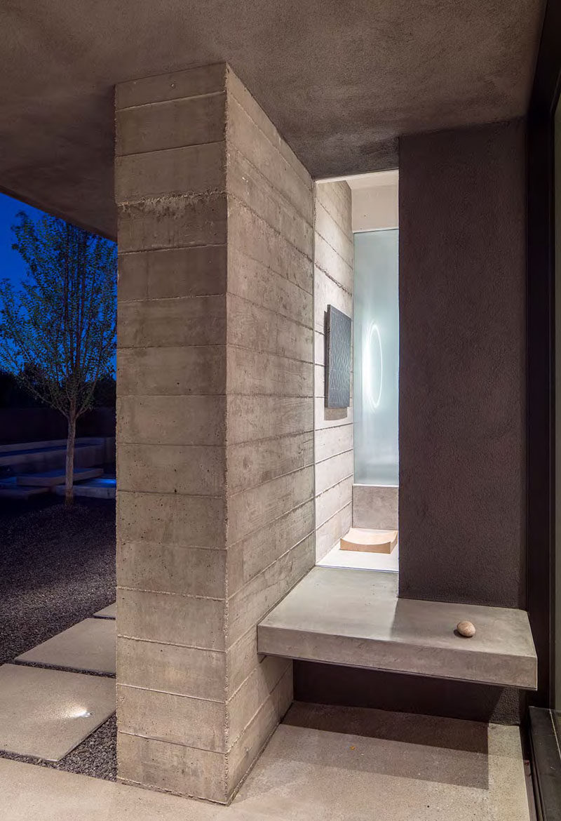 Just before walking through the front door of this modern house, there's a small built-in concrete bench with a window that gives a glimpse of the interior.