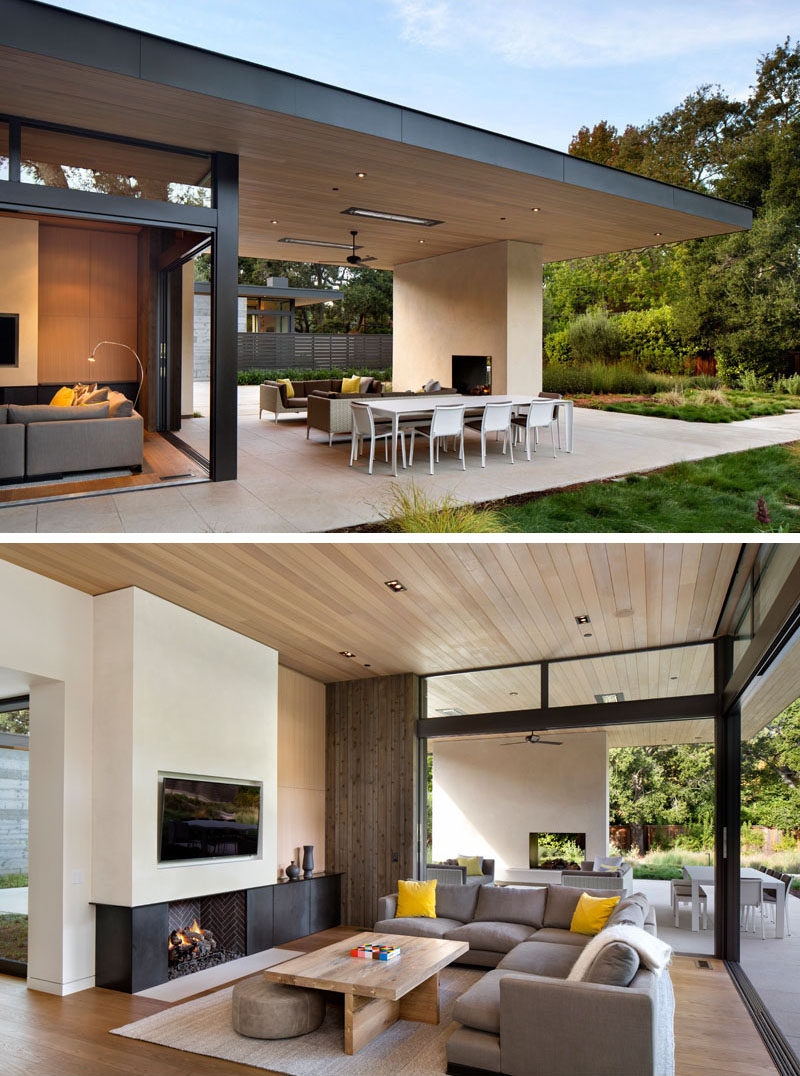 This modern house has been designed to enable indoor/outdoor living with the inclusion of sliding glass doors that open up the living room to the covered outdoor patio. This creates an easy flow from the patio, with its fireplace and lounge area, into the living room with a sectional sofa, wood paneling, and a TV that's been set back slightly into the wall.