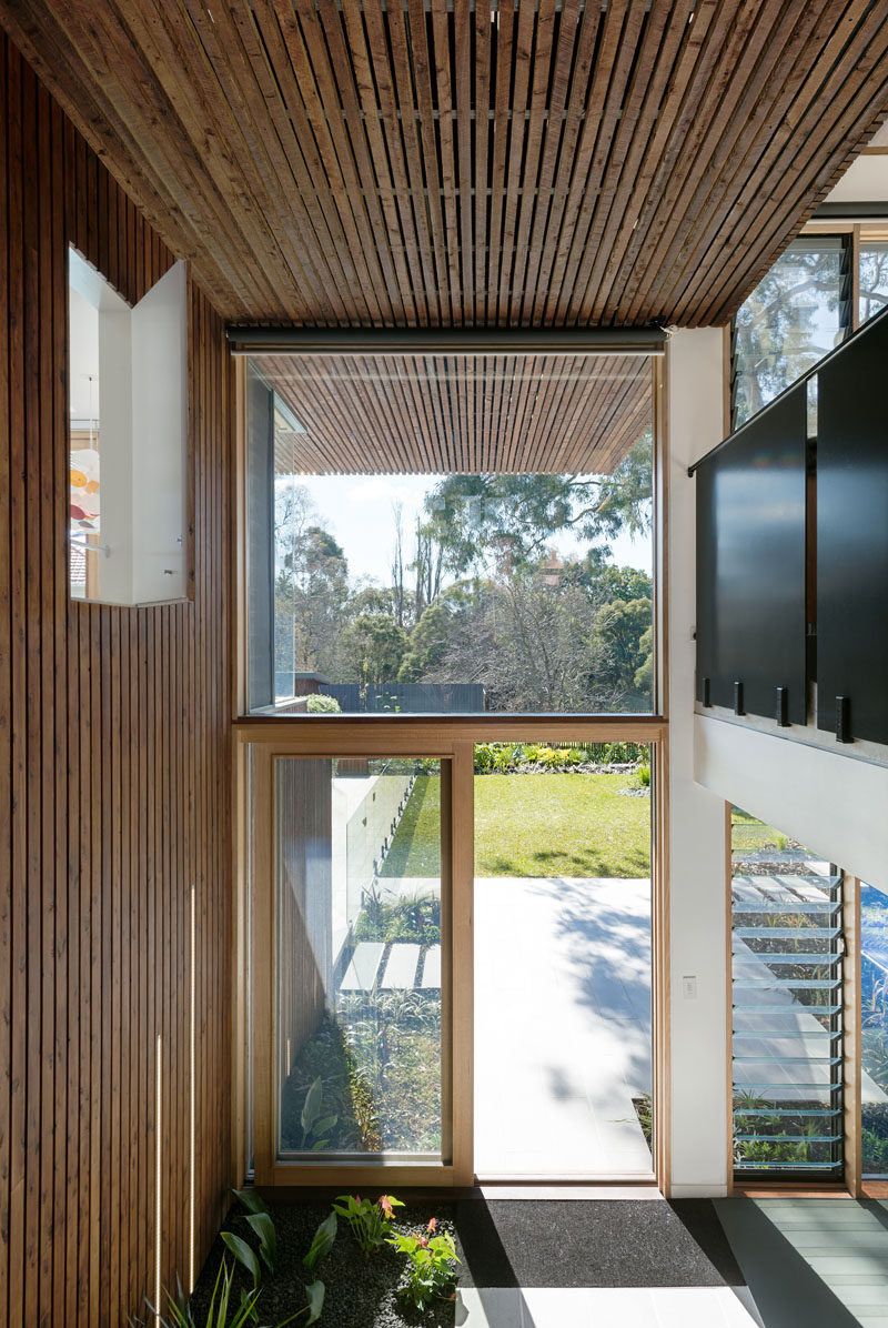 Entering from the back of this modern house, you can see how the wood strips continue from the outside of the house through to the interior, creating design continuity between inside and out. You can also see how large windows take advantage of the landscape outside and use the natural light to brighten the home.