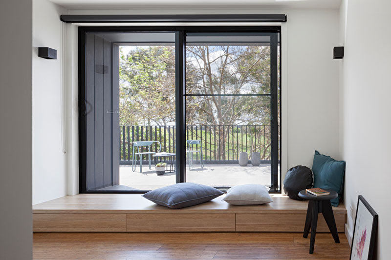 At the top of the stairs in this modern home is a small area with access to a balcony. A small wooden bench acts as a step and a quiet place to relax and look out to the park.