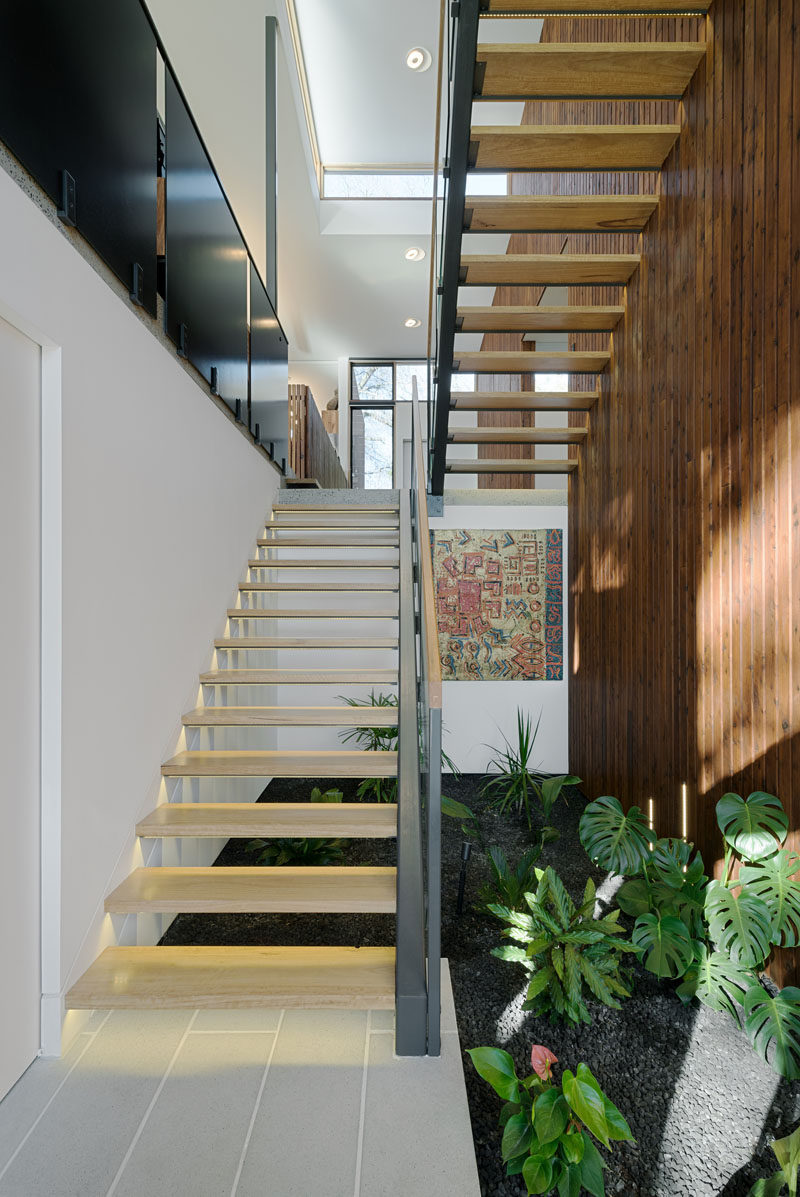 Light wood and steel stairs with hidden lighting underneath each tread creates a safe staircase that leads up to the main level of the home, and below the stairs is a small interior garden.