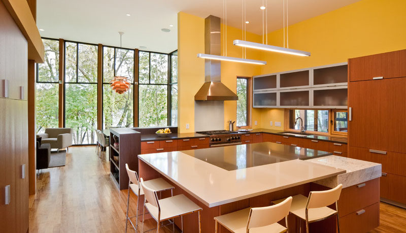 Inside this modern house, a yellow kitchen with wood cabinets and a large kitchen island has lots of surface area for prepping food.