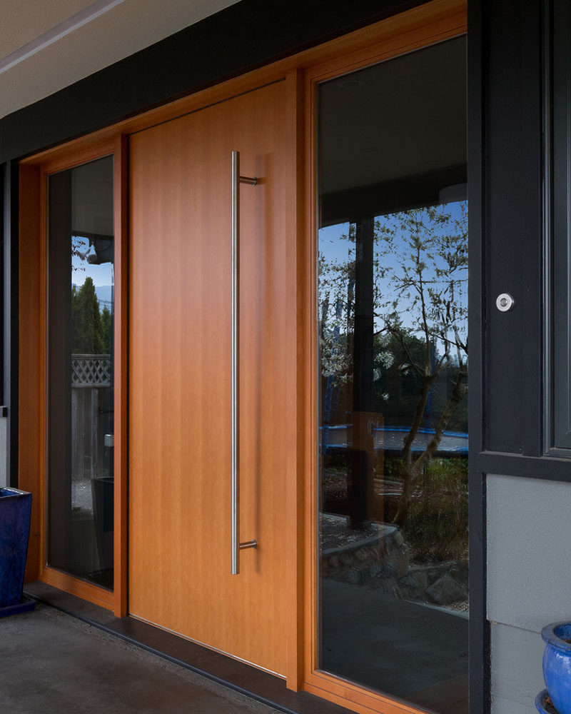 This light wood door features an oversized metal door handle and is flanked by windows on both sides to create a modern entry into this family home.