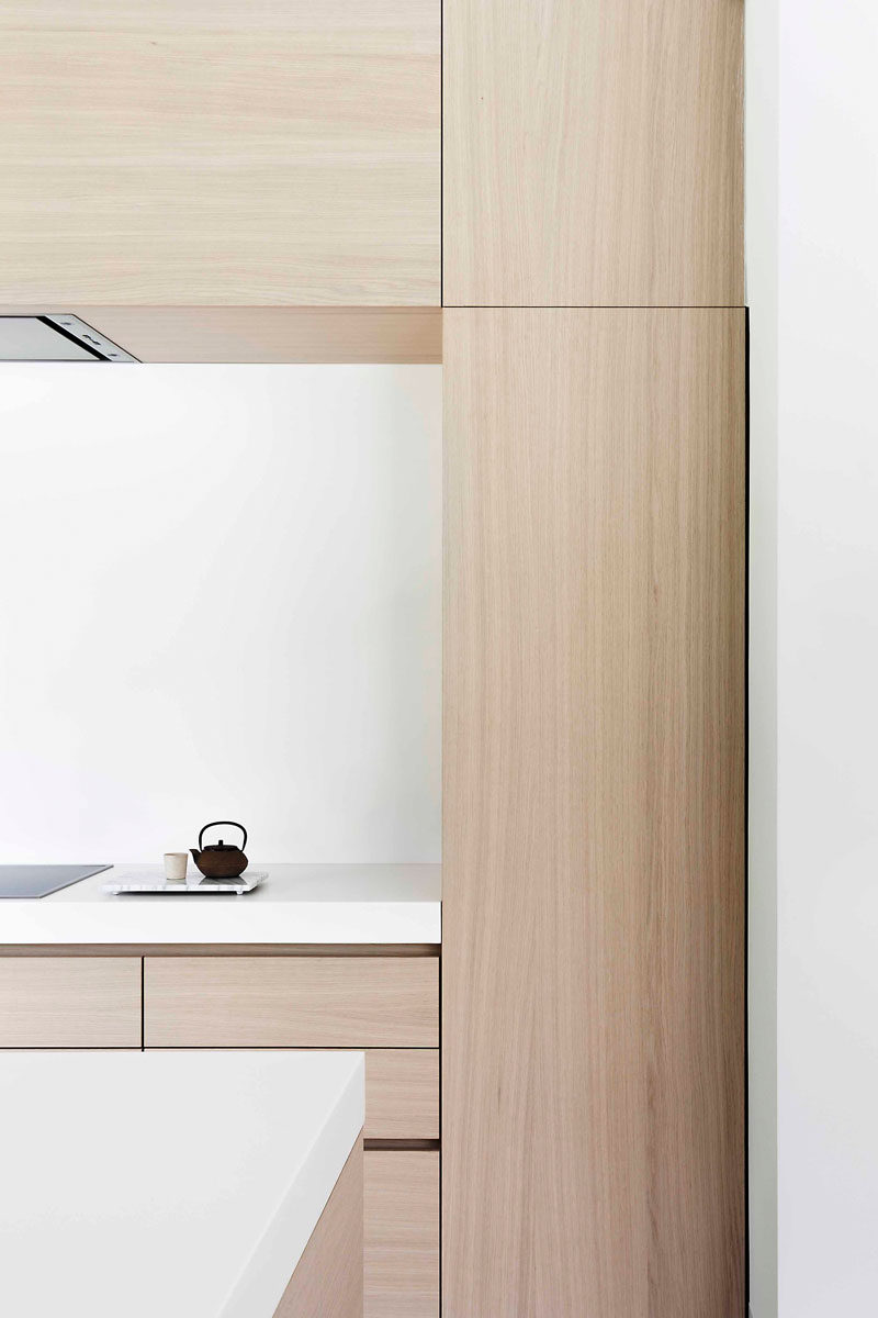 In this modern light wood and white kitchen, the cabinets are mostly free of hardware. Recessed grooves on the sides of cabinets contribute to the overall clean and minimalist feel while keeping it fully functional and easy to maneuver.