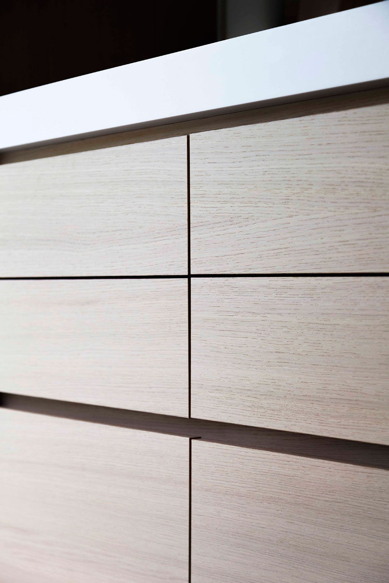 In this modern light wood and white kitchen, hardware-free drawers have recessed grooves along the edge to make them easy to open.