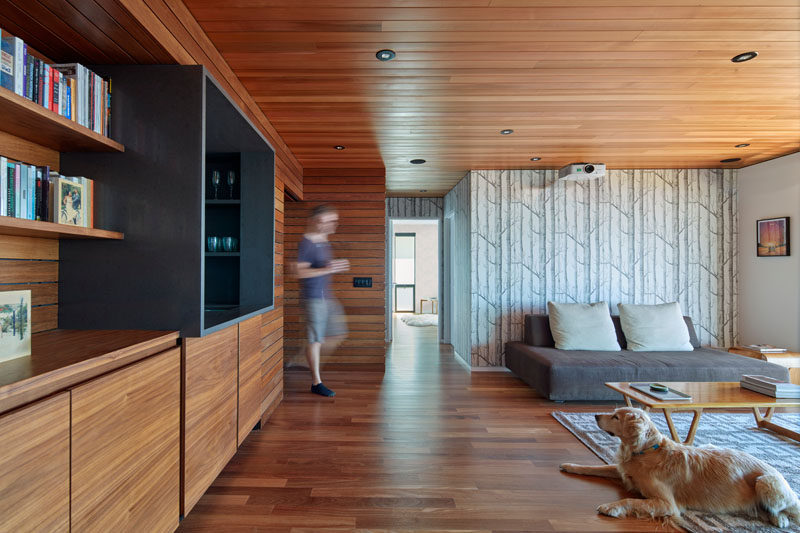 This modern living room features wood ceilings and floors as well as custom wood cabinets. A simple wood tree wallpaper creates a feature wall.