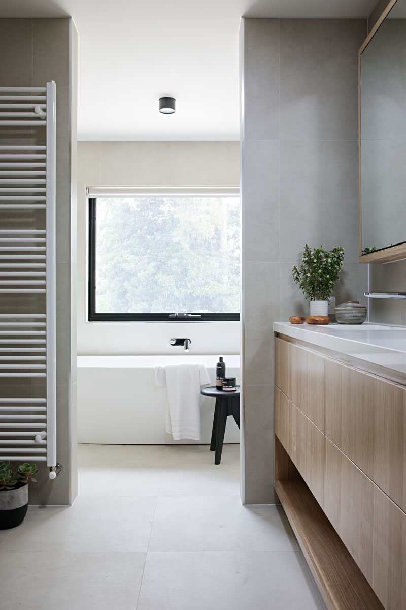 In this modern bathroom, a light wood vanity and plants add a natural touch to the grey and white bathroom.