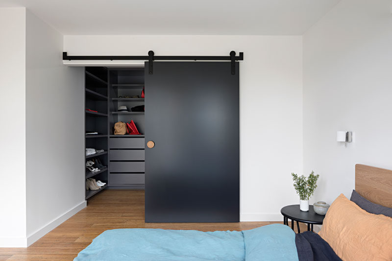 This modern master bedroom has a large walk-in closet hidden behind a matte black sliding barn door.