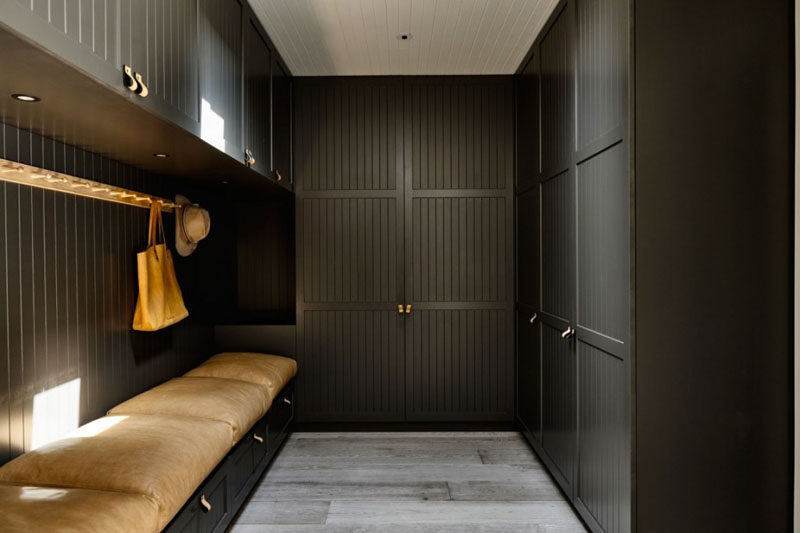 In this modern mudroom, large overstuffed light brown leather pillows cushion the built-in bench with storage, while black cabinets with leather drawer pulls provide plenty of storage and organization opportunities. For hanging hats and bags, there's a simple light wood wall mounted coat rack.
